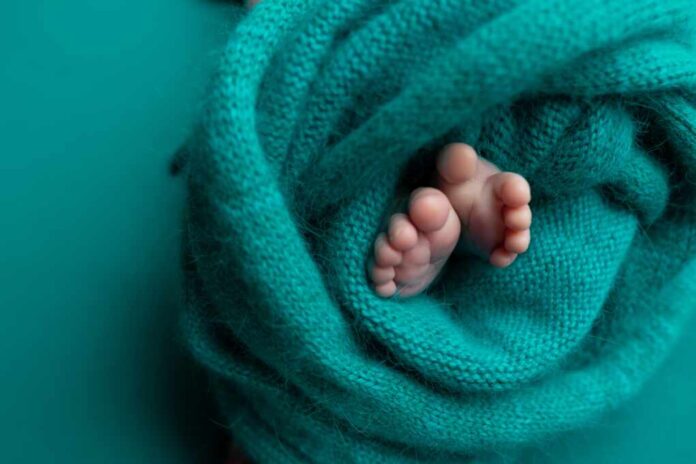 The,Baby's,Legs,Are,Wrapped,In,A,Turquoise,Knitted,Blanket.