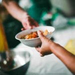 A person handing a bowl of food to another person in a communal setting
