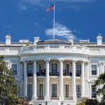 The White House with an American flag flying against a blue sky