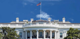 The White House with an American flag flying against a blue sky