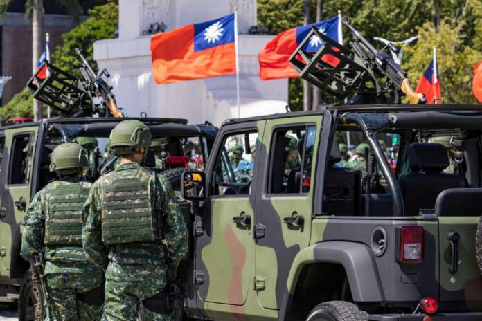 Soldiers in camouflage uniforms standing near military vehicles with flags in the background