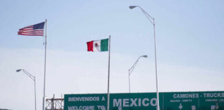 Flags of the United States and Mexico at a border crossing with a welcome sign