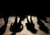 Silhouettes of people walking on a street, casting long shadows