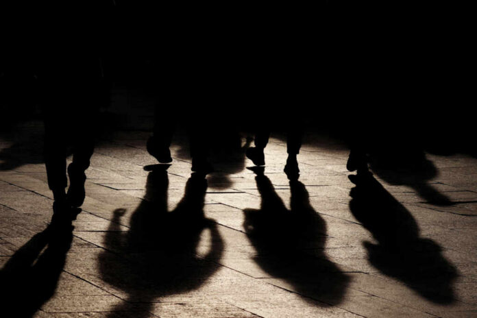 Silhouettes of people walking on a street, casting long shadows