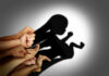 A collection of hands creating a shadow silhouette of a fetus