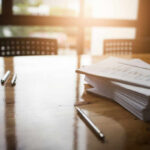 An office workspace with documents, glasses, and pens on a wooden table