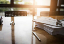 An office workspace with documents, glasses, and pens on a wooden table