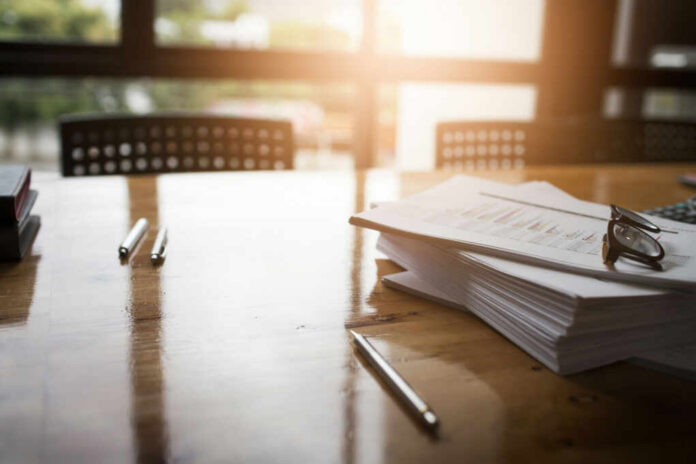 An office workspace with documents, glasses, and pens on a wooden table