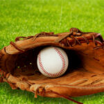 A baseball glove with a baseball resting inside, set on green grass
