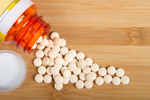 Spilled white pills from a prescription bottle on a wooden surface
