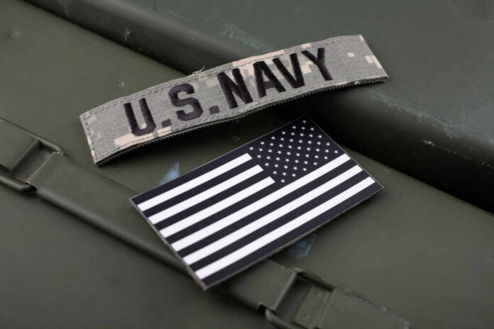 shutterstock_2325992831.jpg U.S. Navy patch and American flag on a green surface