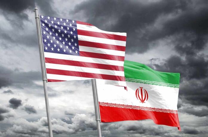 shutterstock_2418578685.jpg Flags of the United States and Iran waving against a cloudy sky