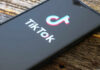 Close-up of a smartphone displaying the TikTok logo on a wooden surface