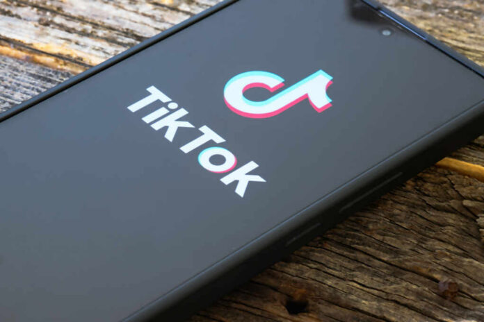 Close-up of a smartphone displaying the TikTok logo on a wooden surface
