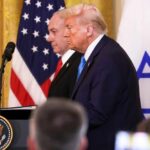 Donald Trump and another official at a press conference with flags in the background