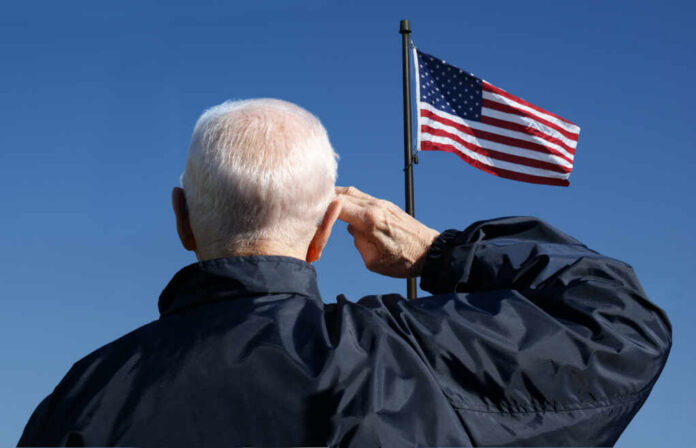 shutterstock_772898548.jpg Elderly man saluting in front of an American flag against a blue sky