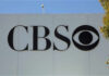 CBS logo displayed on a white wall with a blue sky background