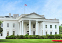The White House with an American flag flying above, surrounded by greenery