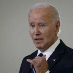 A man in a suit gesturing while speaking during a public address