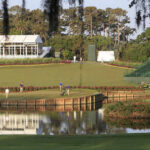 A scenic view of a golf course with players and maintenance equipment near a water feature