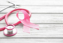 A pink ribbon next to a stethoscope on a wooden surface