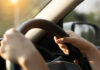 Hands gripping a steering wheel inside a car with sunlight streaming in