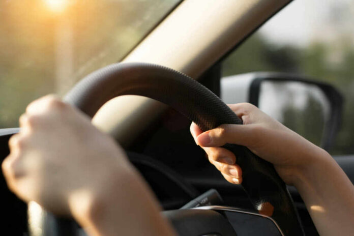 Hands gripping a steering wheel inside a car with sunlight streaming in