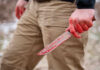 A person holding a bloody knife in an outdoor setting
