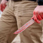A person holding a bloody knife in an outdoor setting