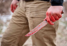 A person holding a bloody knife in an outdoor setting
