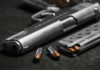 Close-up of a handgun with bullets and a magazine on a dark surface