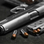 Close-up of a handgun with bullets and a magazine on a dark surface