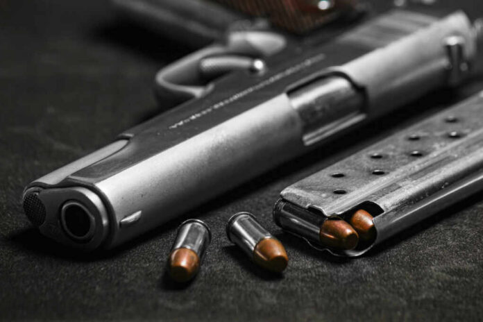 Close-up of a handgun with bullets and a magazine on a dark surface