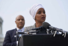 Ilhan Omar speaking at a press conference with André Carson in the background