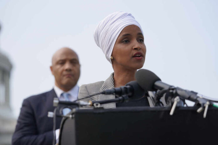Ilhan Omar speaking at a press conference with André Carson in the background