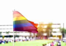 Rainbow flag waving in the foreground with a blurred crowd in the background