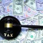 A gavel with the word 'TAX' on it placed on a background of US dollar bills
