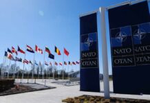 Flags of various nations displayed outside NATO headquarters under a clear blue sky