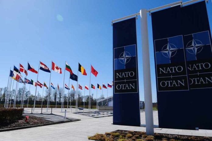 Flags of various nations displayed outside NATO headquarters under a clear blue sky