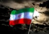Iranian flag waving against a dark, cloudy sky