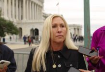 A woman with long blonde hair stands outdoors, surrounded by people holding smartphones.