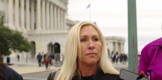 A woman with long blonde hair stands outdoors, surrounded by people holding smartphones.