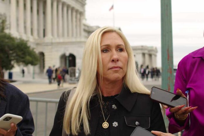A woman with long blonde hair stands outdoors, surrounded by people holding smartphones.
