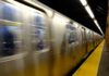 A subway train in motion at a station with blurred reflections