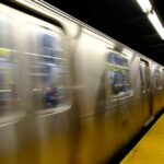 A subway train in motion at a station with blurred reflections