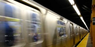 A subway train in motion at a station with blurred reflections