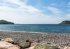 A rocky beach with colorful pebbles and a view of the ocean and green hills under a blue sky