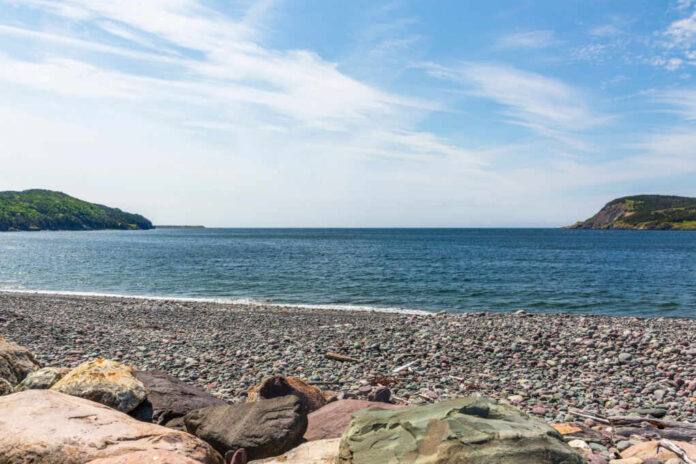 A rocky beach with colorful pebbles and a view of the ocean and green hills under a blue sky