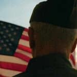 A veteran in uniform standing in front of an American flag during sunset