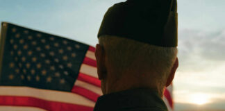 A veteran in uniform standing in front of an American flag during sunset